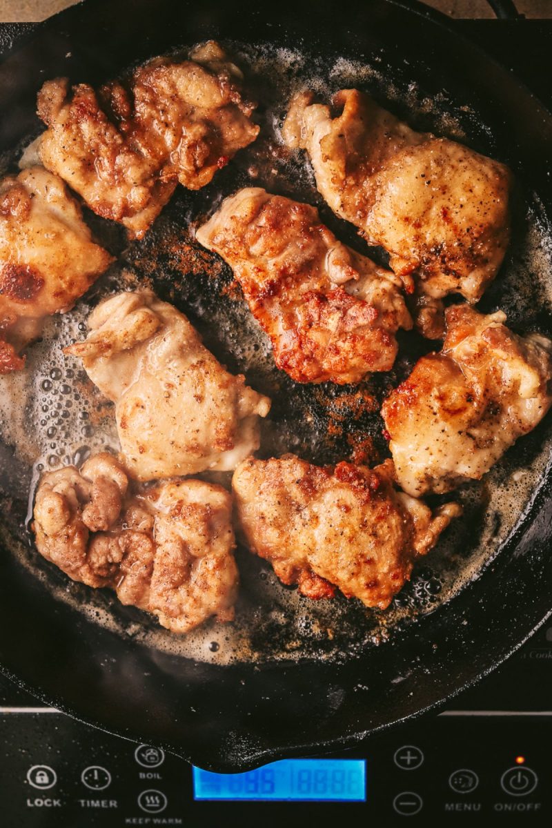 Champagne chicken fried in a skillet on a stovetop.