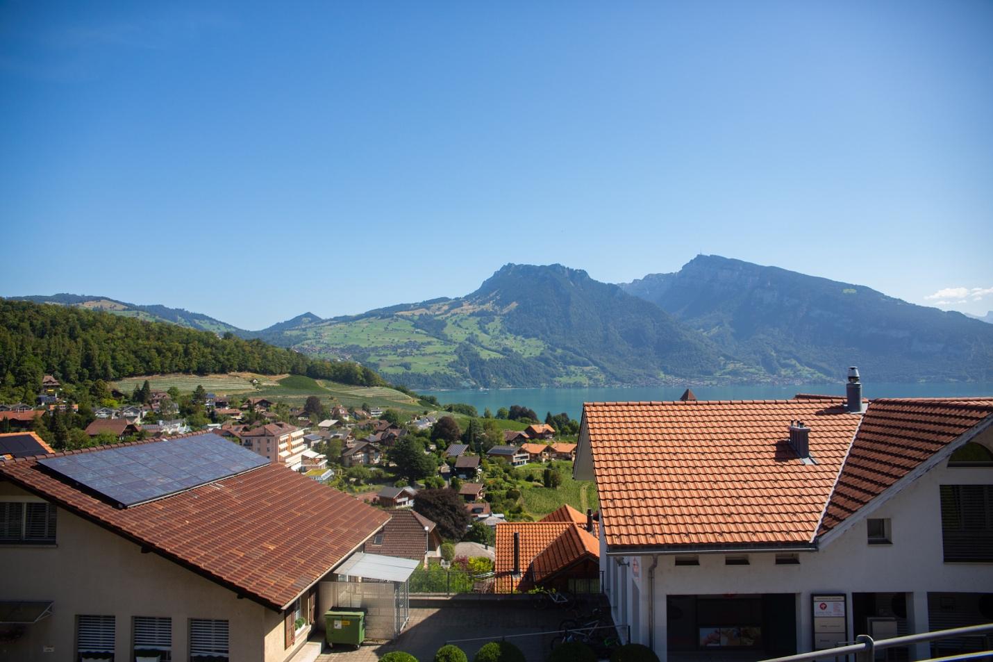 A view of a town with a lake and mountains in the background

Description automatically generated