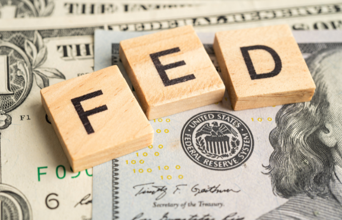 Wooden blocks spelling "FED" on US dollar bills, hinting at Federal Reserve policies impacting the real estate market.