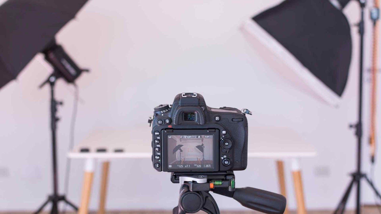 A digital camera on a tripod, set against a photography studio setup with lighting equipment.