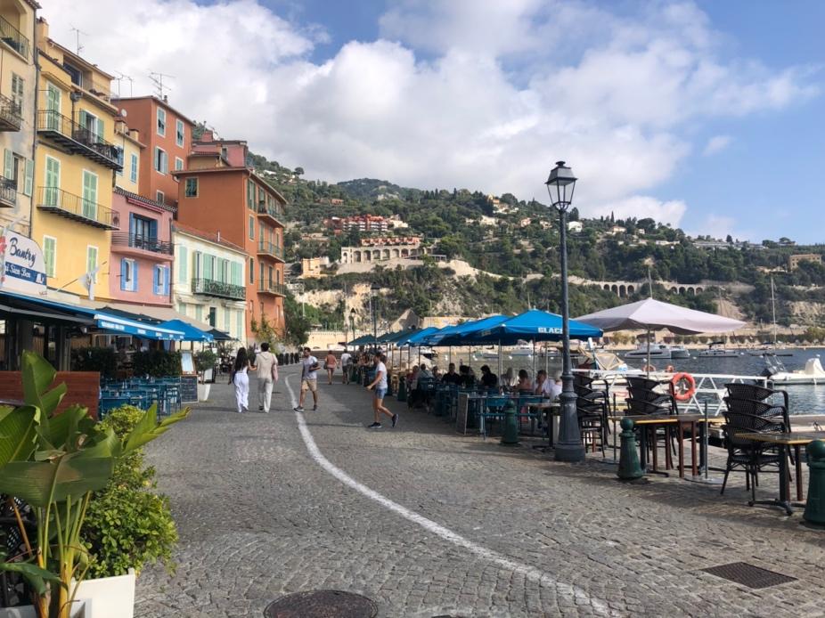 A street with tables and umbrellas and buildings on the side

Description automatically generated