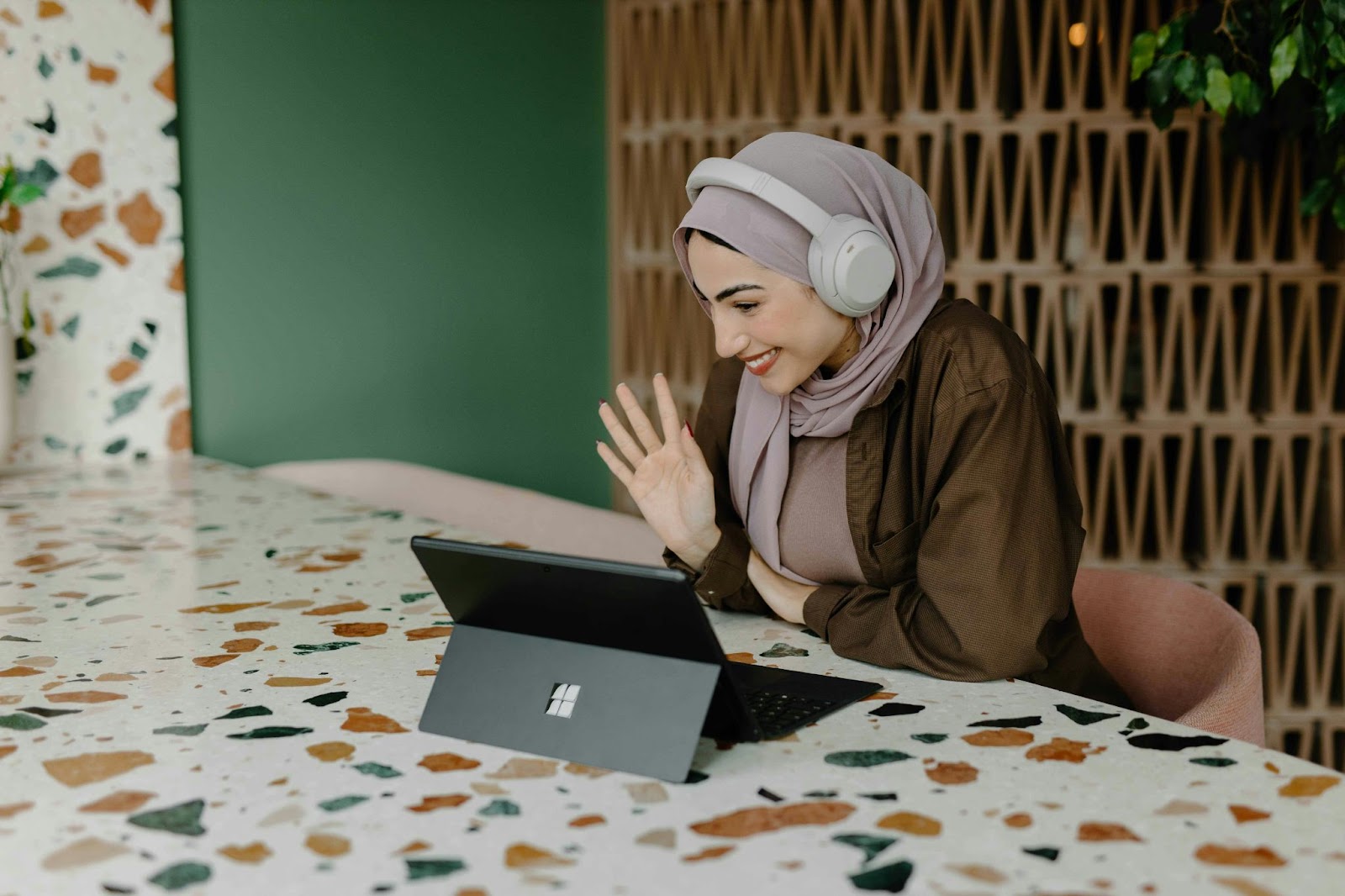 A woman wearing headphones, smiling and waving to a (potential) client on the other side of the tablet screen.