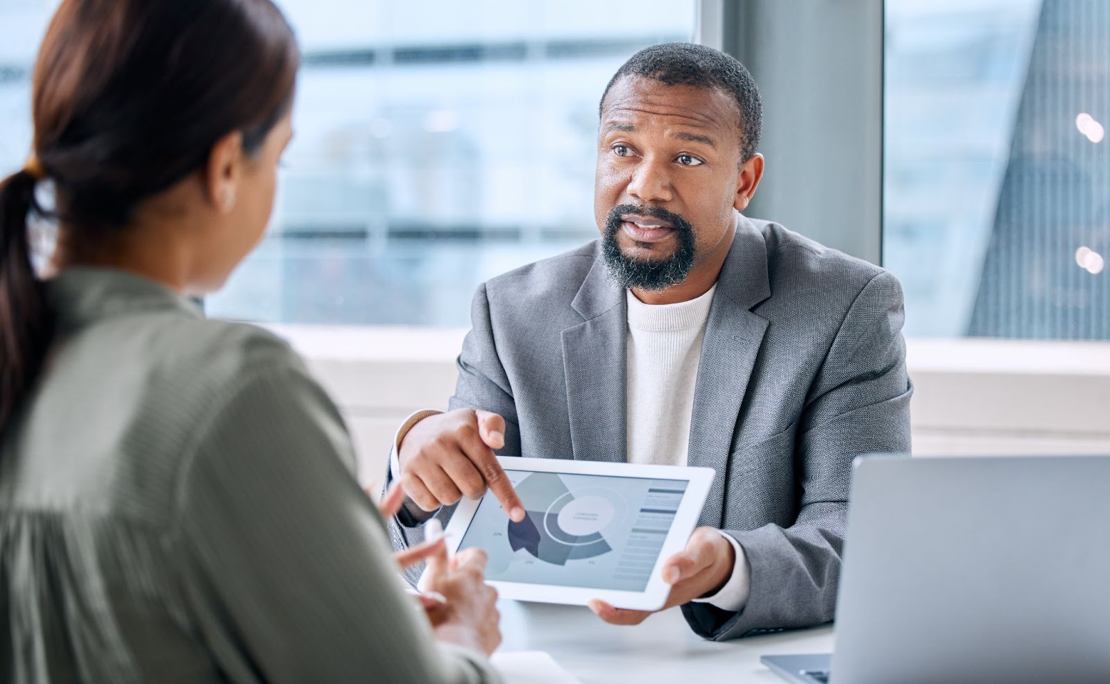 A male financial consultant in a gray suit with a mustache highlights financial issues in reports to his female client.