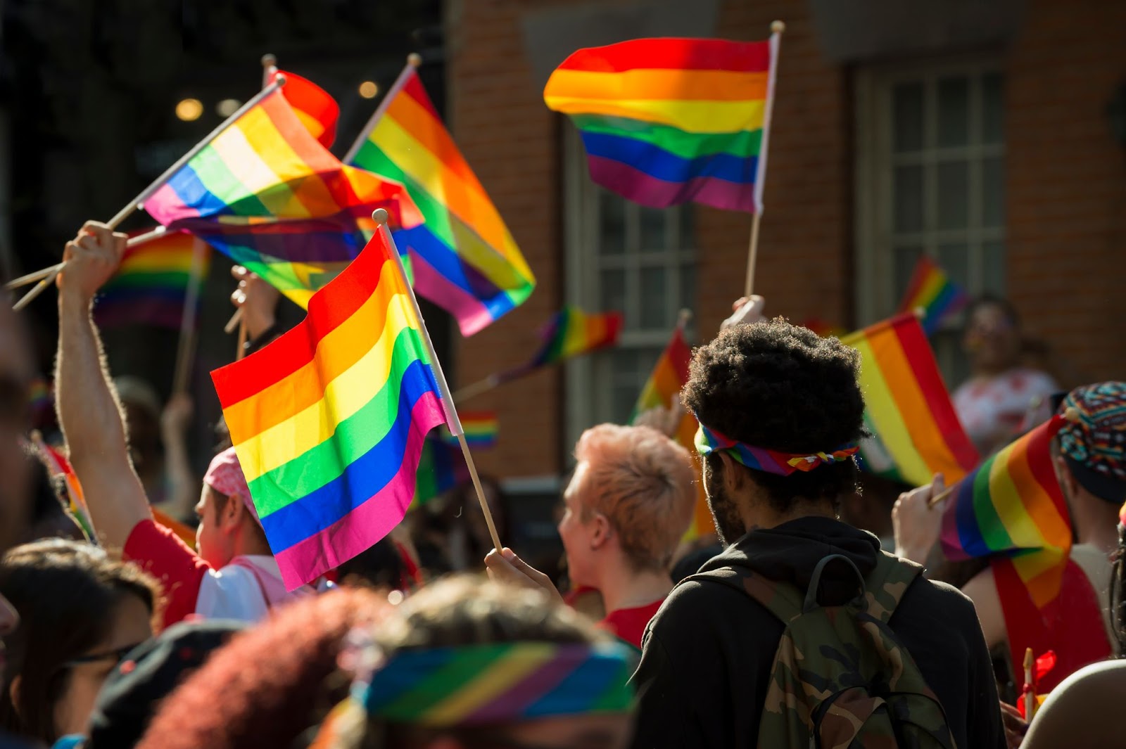 Pessoas na rua com diversas bandeiras da comunidade LGBT+ levantadas acima de suas cabeças.