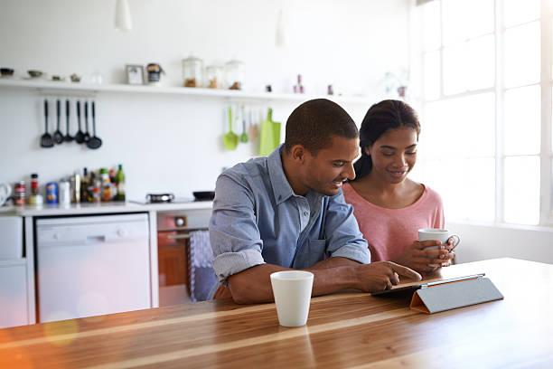 Enjoying a morning internet catch up together Shot of a young couple sitting at their dining table using a digital tablet black couple talking in kitchen stock pictures, royalty-free photos & images