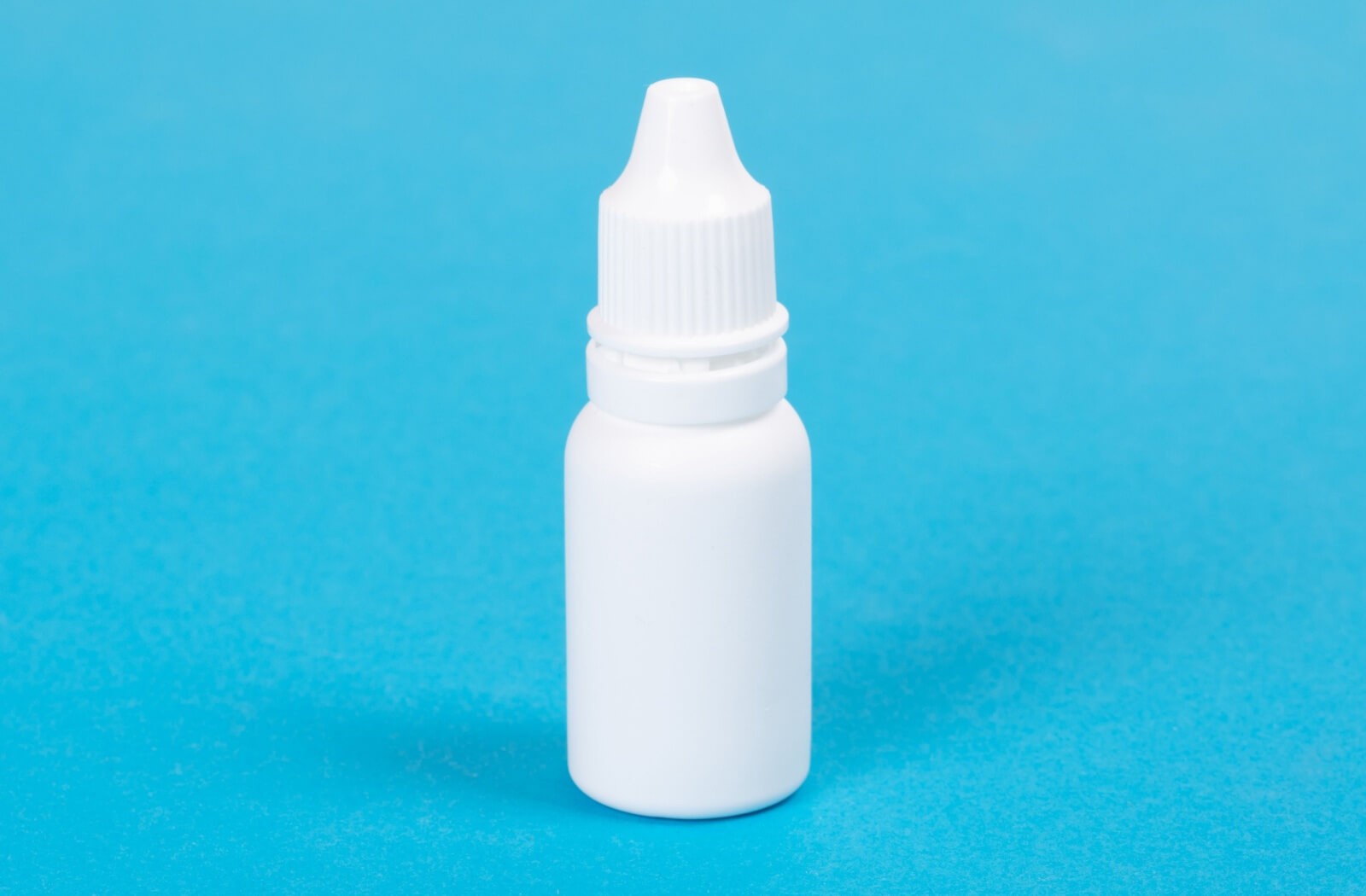 A close-up of a bottle of eyedrops against a blue background.