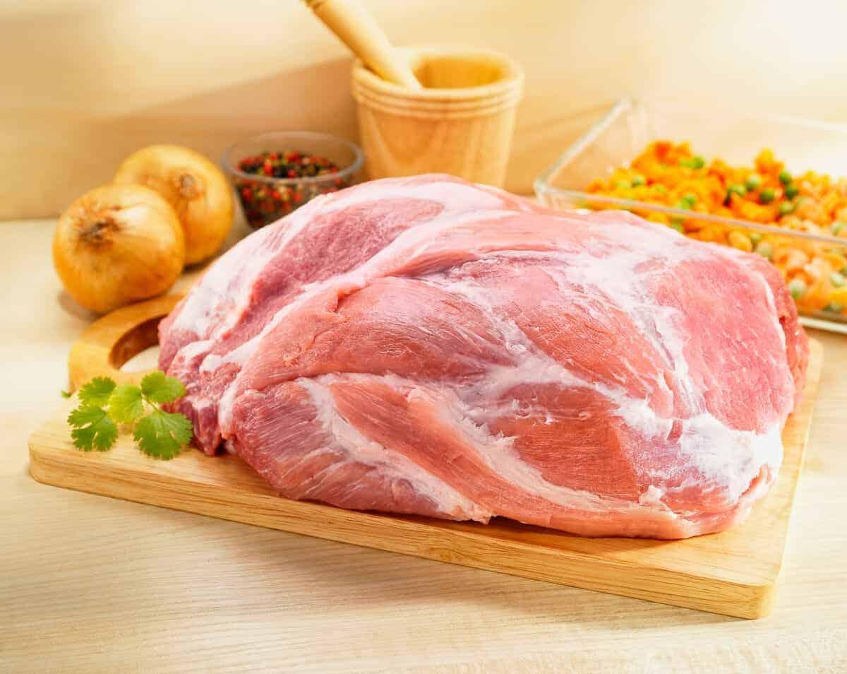 O șuncă de picnic crudă de porc pe o masă de tăiat cu ceapă și ierburi
