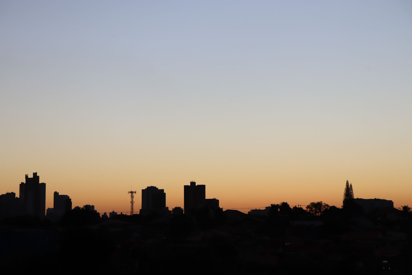 Paisagem da cidade de Londrina ao entardecer. Prédios de diferentes tamanhos contra a luz, com céu azul passando para o alaranjado no horizonte.