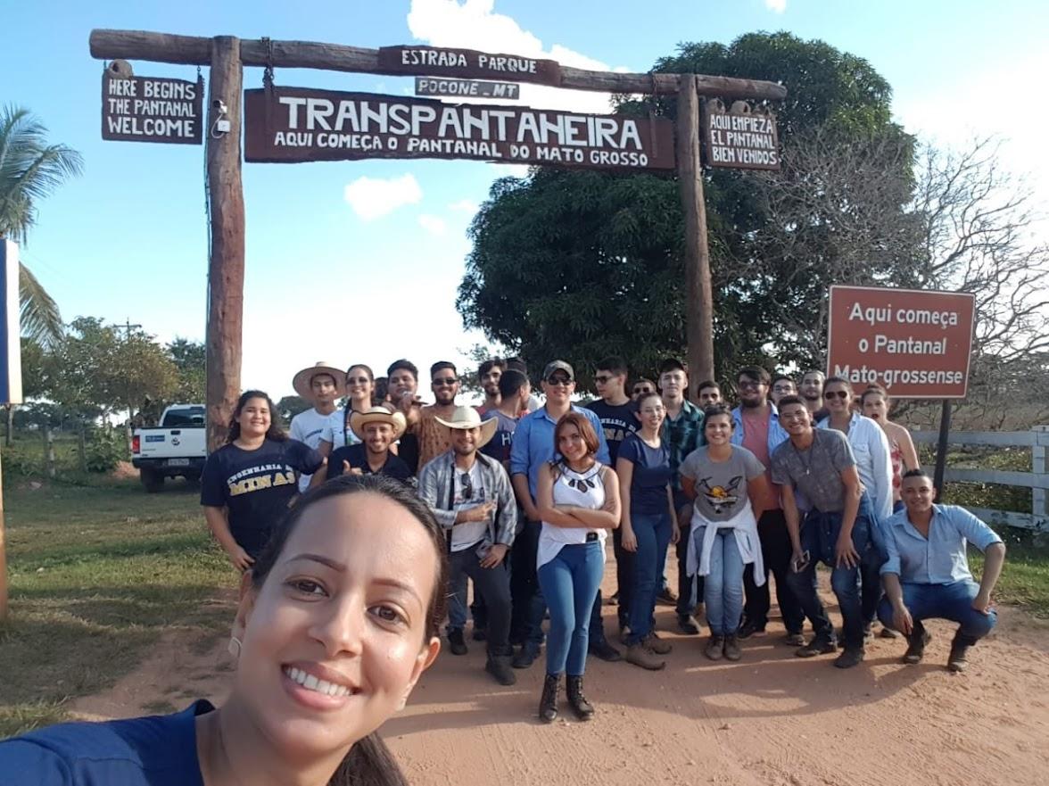 Grupo de pessoas posando para foto em frente a placa

Descrição gerada automaticamente