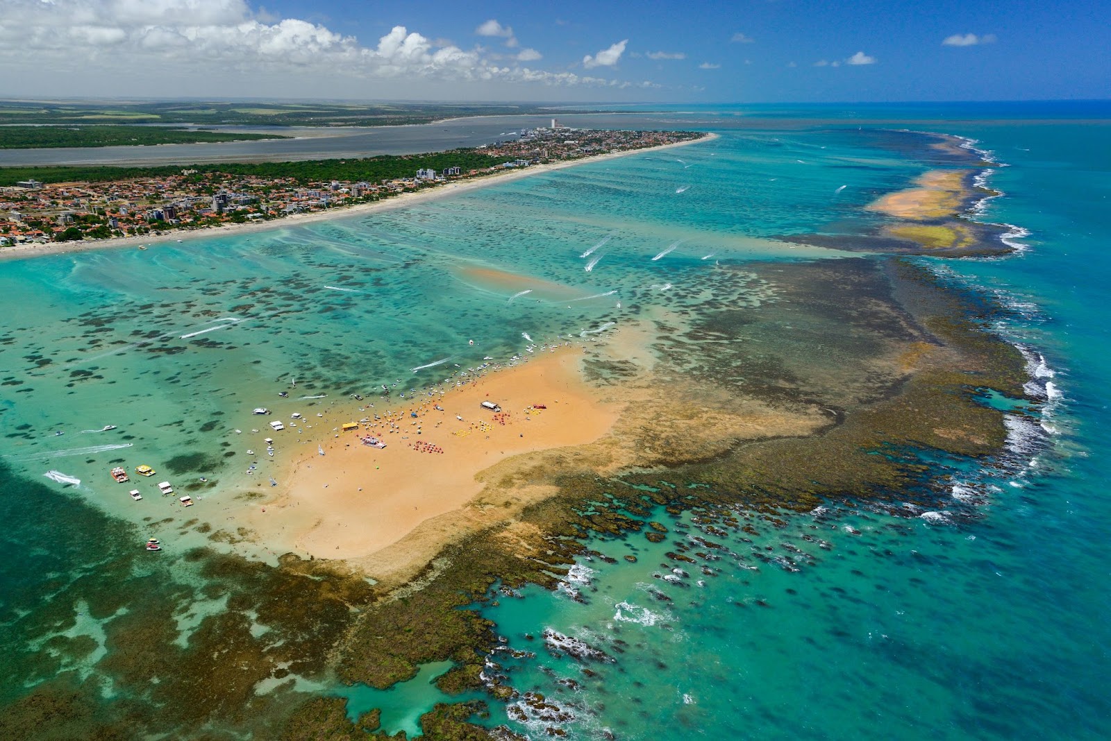 Ilha de Areia Vermelha, uma das famosas praias de João Pessoa. O longo banco de areia alaranjada fica em meio ao azul intenso do mar, não muito distante do continente. É possível ver algumas embarcações na água e banhistas espalhados pela areia