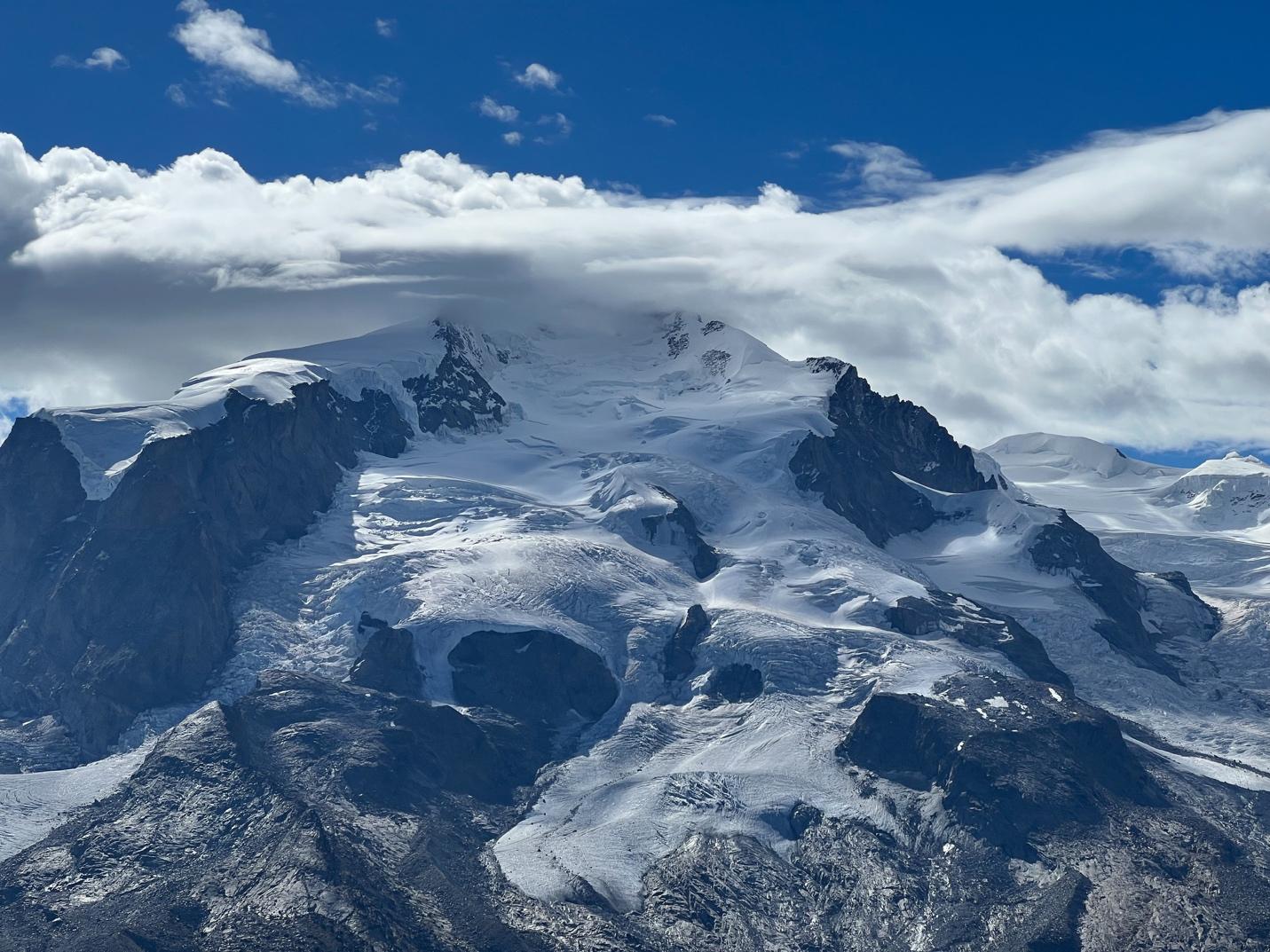 A snowy mountain with clouds in the sky

Description automatically generated