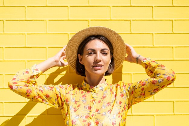 A woman in yellow dress and hat against a yellow wall.