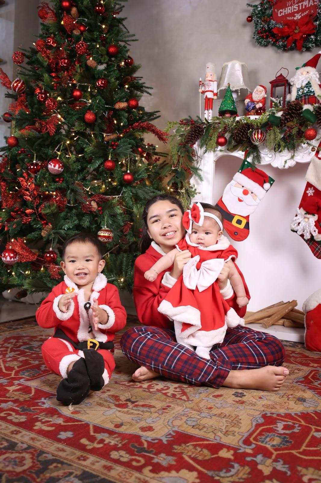 newborn christmas photo idea: newborn dressed up in a Christmas dress posing with older sister wearing Christmas sweater and older brother wearing a Santa outfit