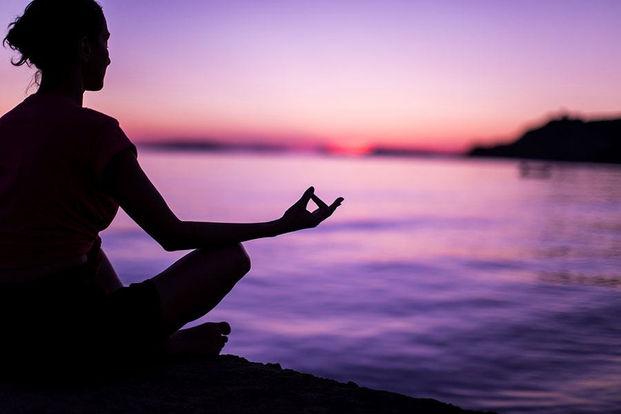 A woman meditating at sunset.
