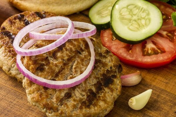 Ground beef patty with onion slices on top, and cucumber, tomatoes, and garlic on the side