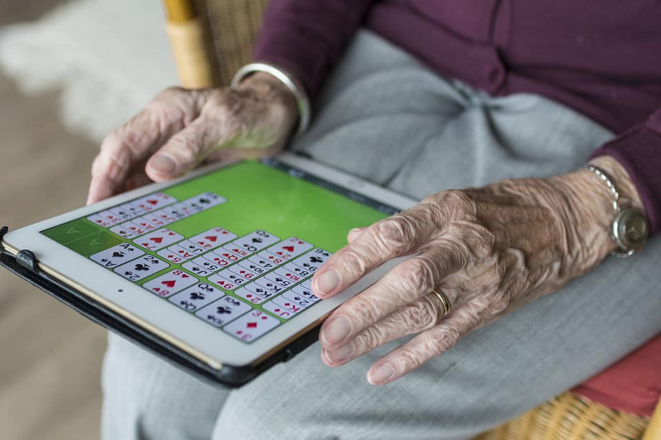 A senior citizen playing solitaire on a mobile tablet