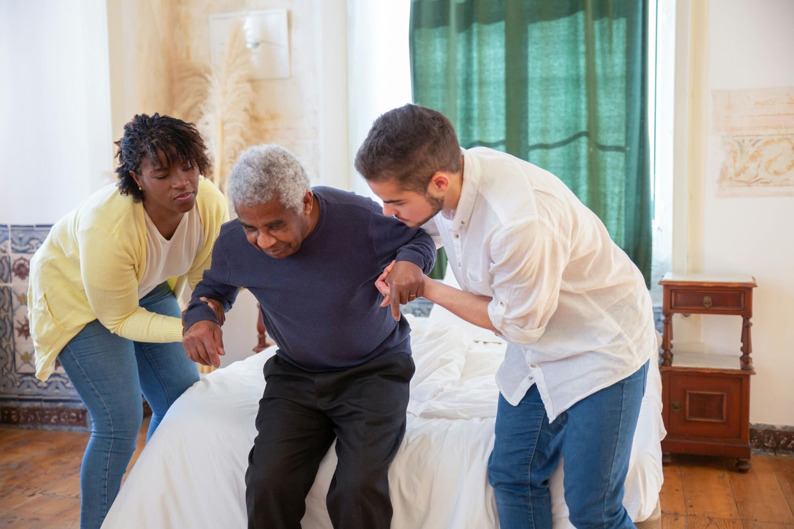 Two caregivers helping a senior citizen out of bed