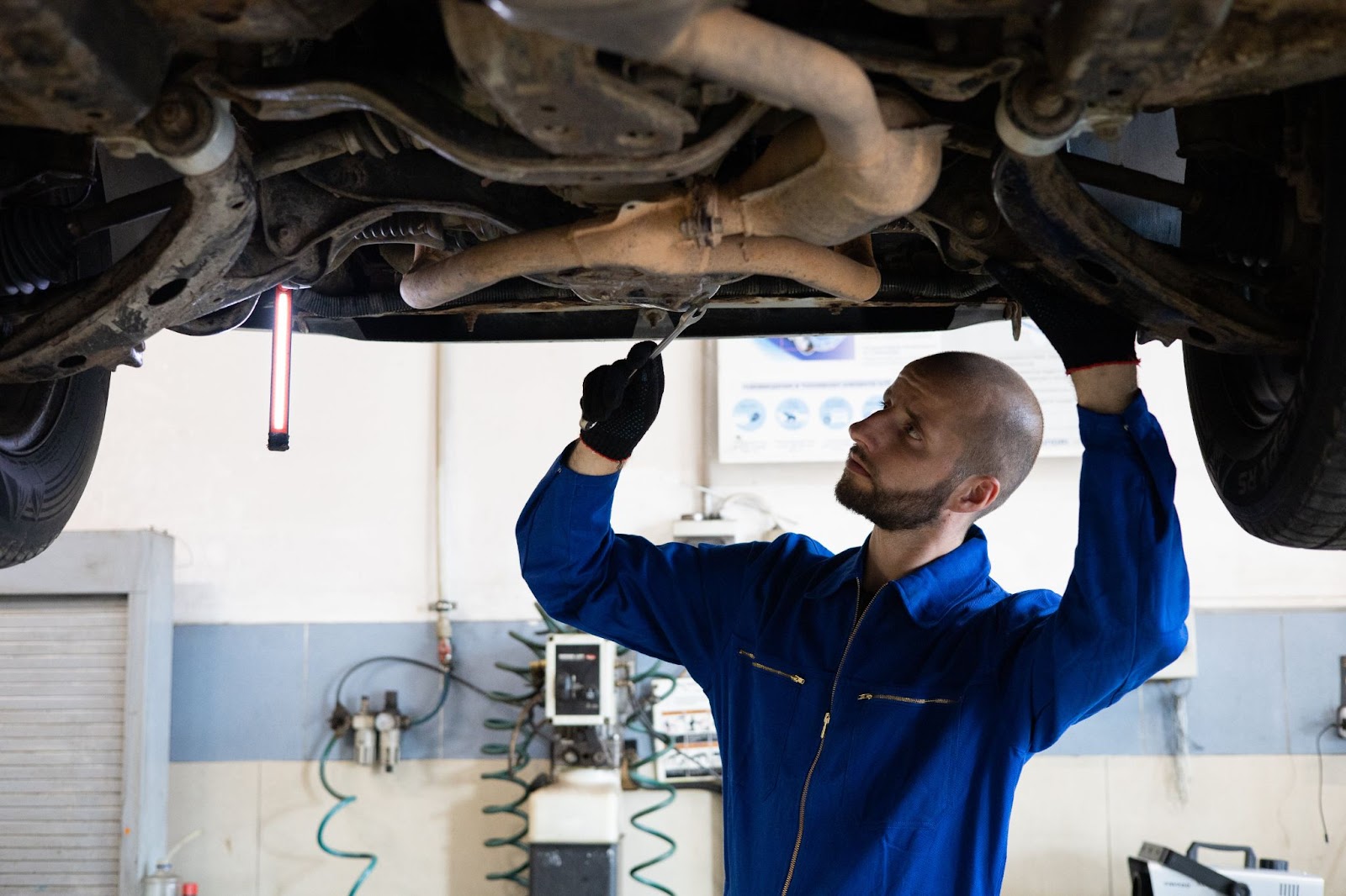 A mechanic underneath a vehicle working on the exhaust pipes underneath the vehicle
