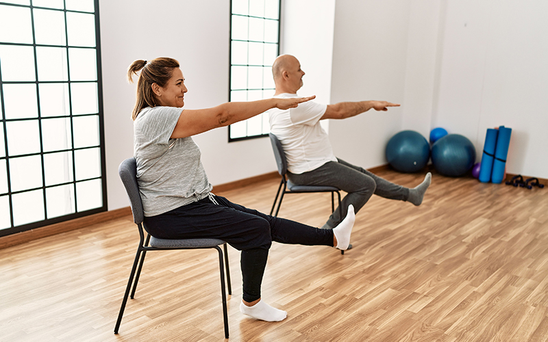 fitness instructor with senior man doing chair yoga