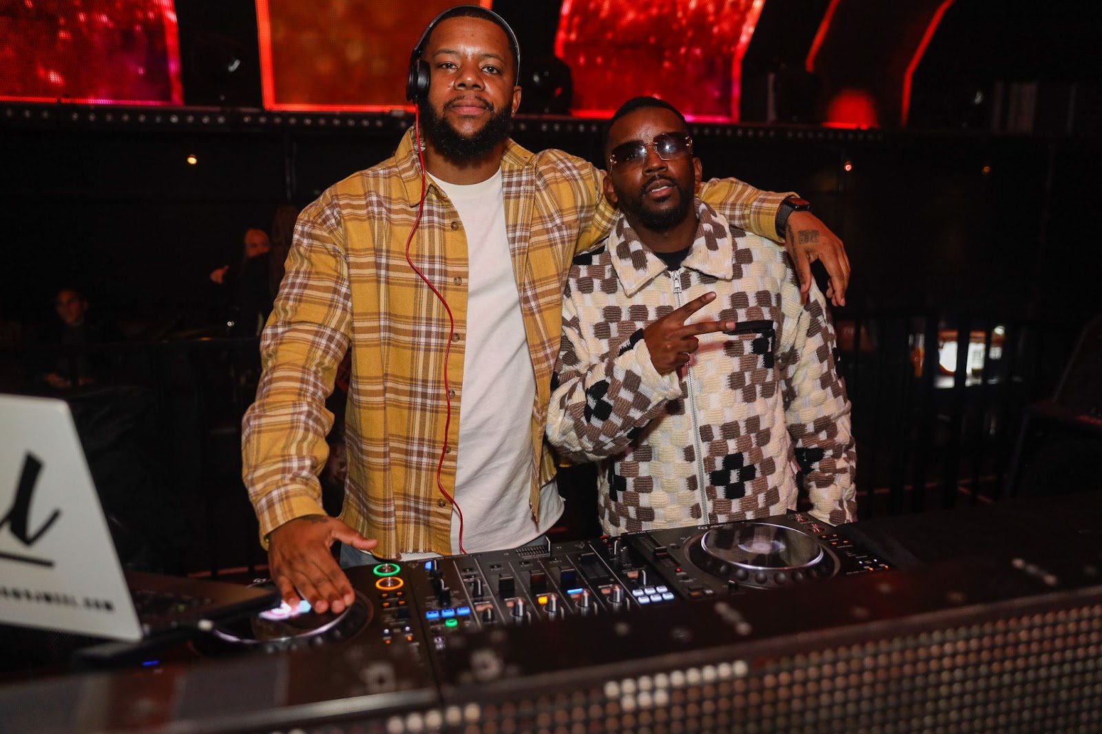 Two Black male DJs posing behind the DJ booth
