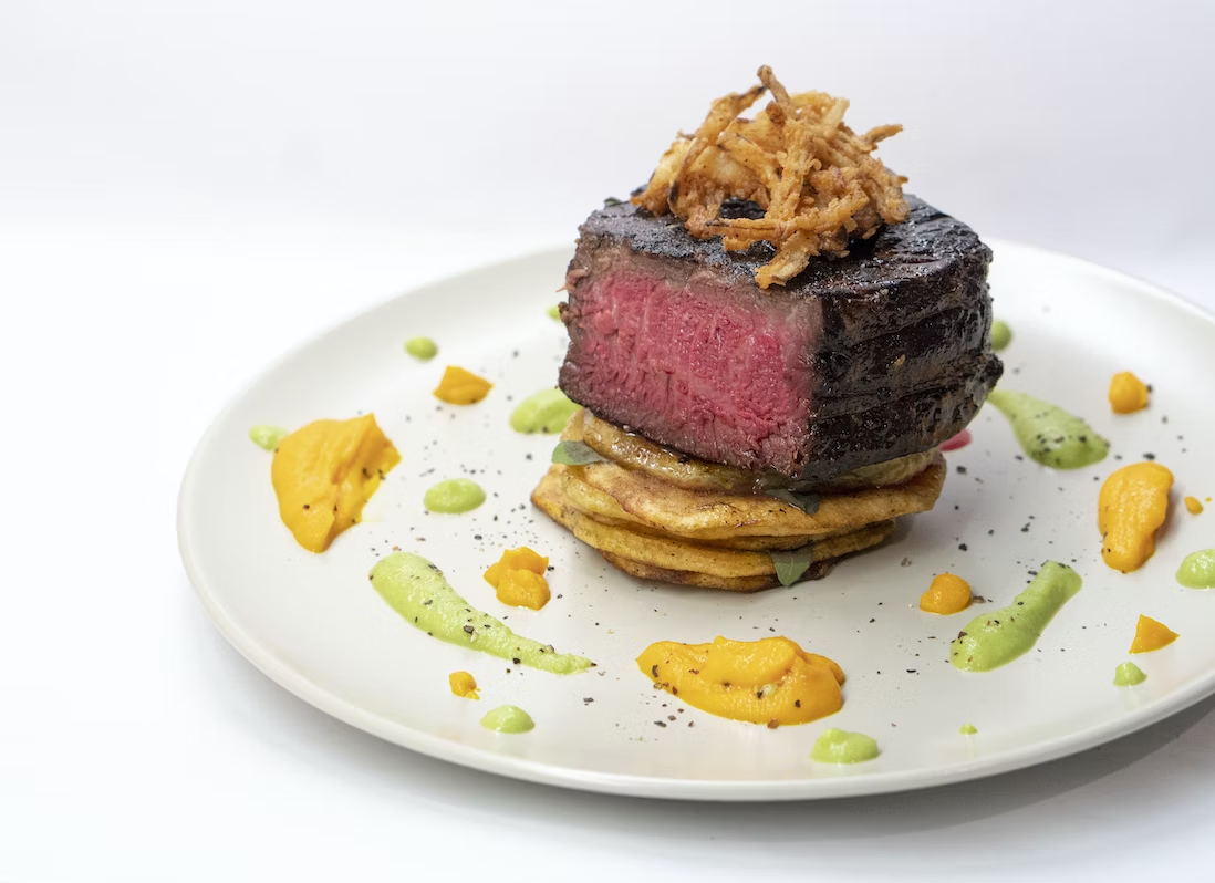 a cut of steak surrounded by sauces on a small plate