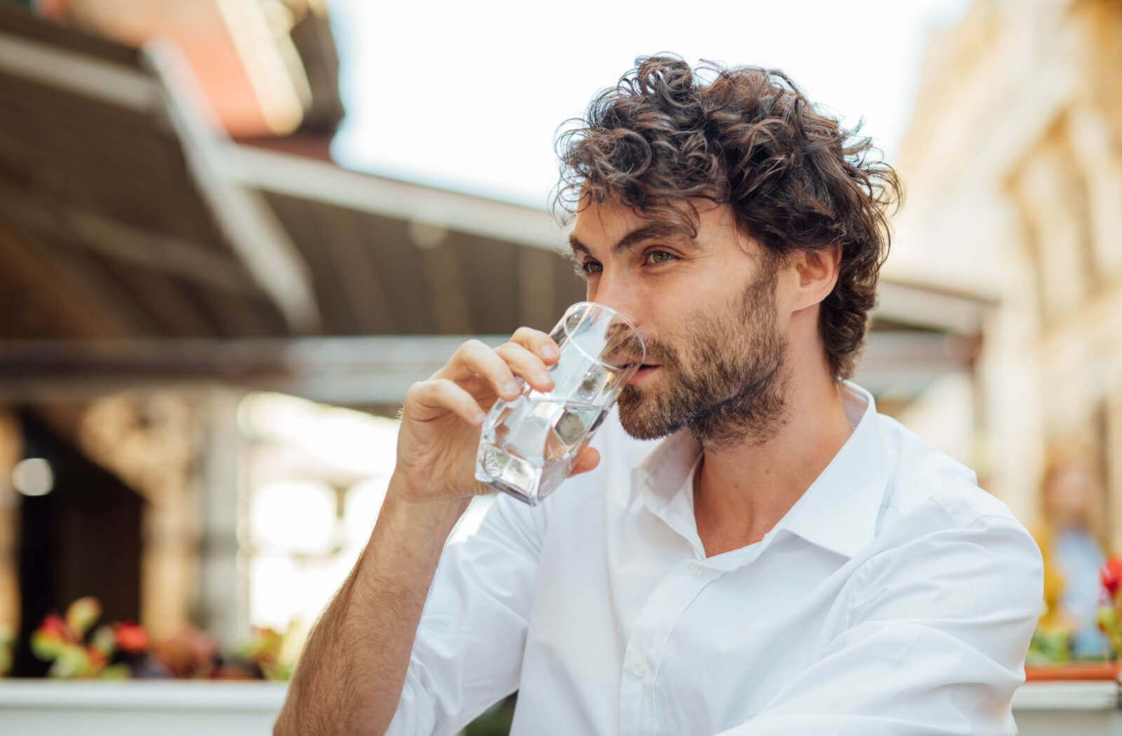 A man in a white shirt drinking a glass of water outdoors.