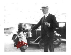 A black and white photo of a young girl selling poppies to an older man. The poppies are red.