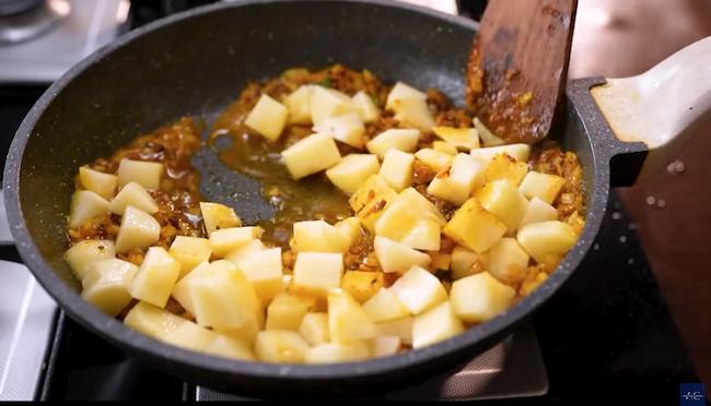 Chopped onions and diced potatoes being mixed into the spiced gravy, cooking until onions turn translucent