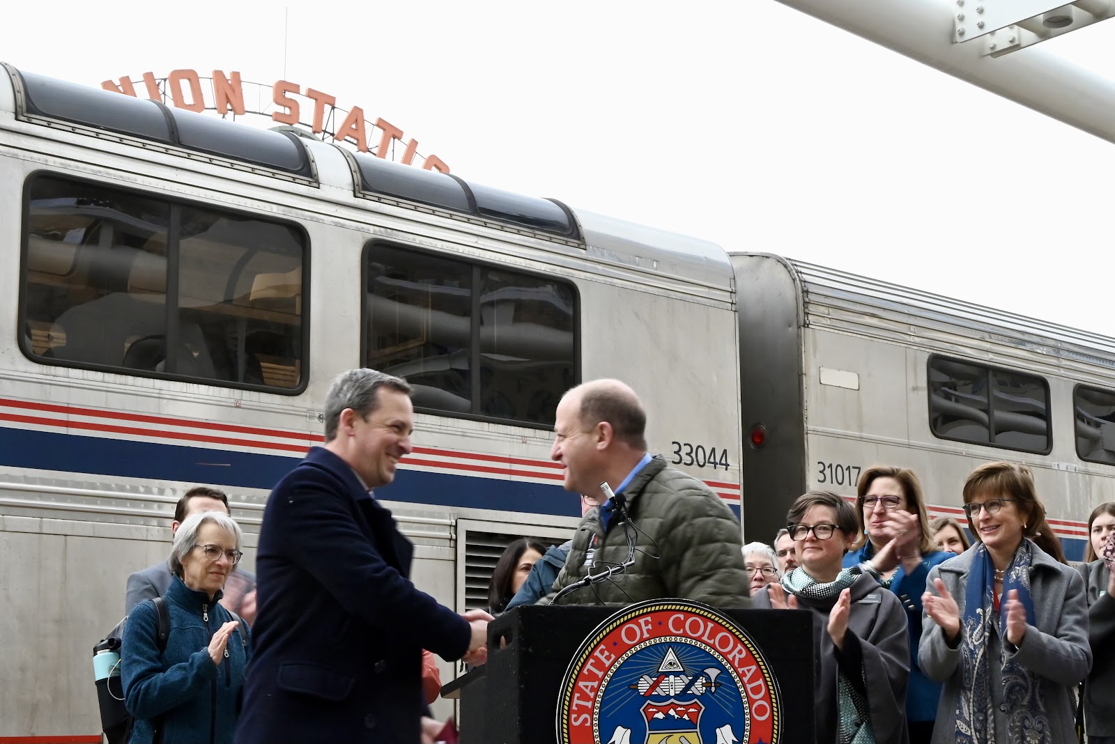 Governor Polis shakes Senate President Fenberg's hand on the train platform.