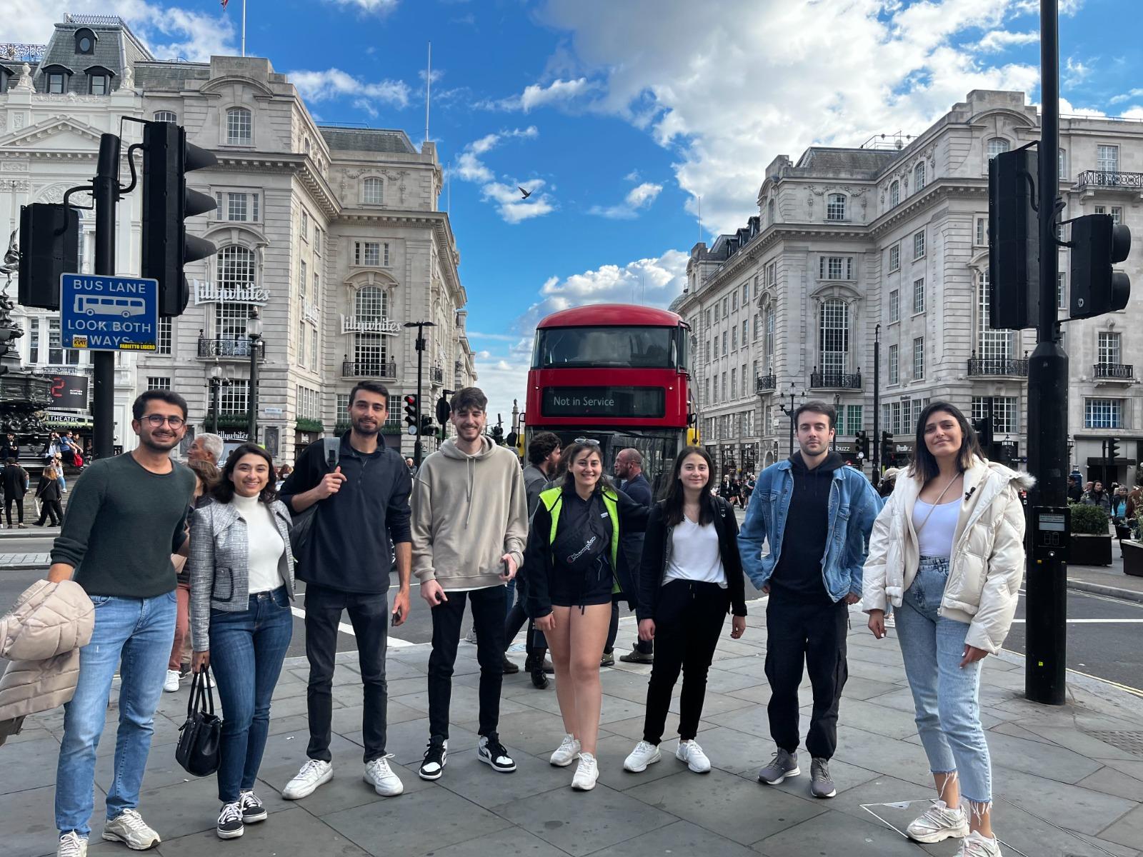 A group of people posing for a photo in front of a red double decker bus

Description automatically generated
