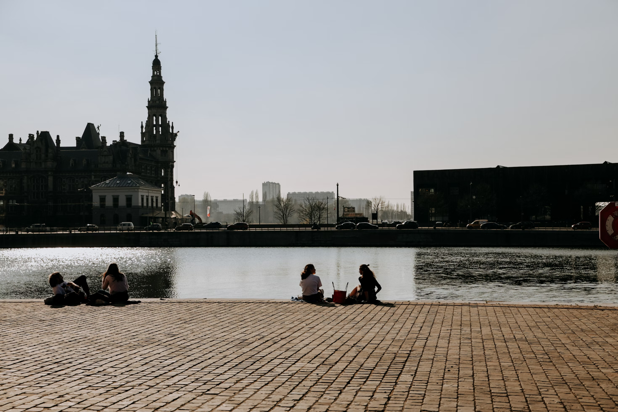 This image shows people sitting by the side of a river in a city.