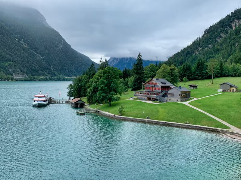 In this image, we can see a house next to a lake or river in the mountains.