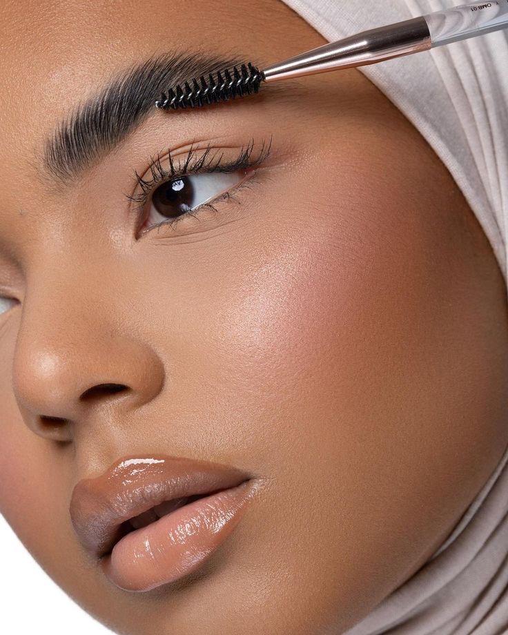 A Muslimah with a hijab on, brushing her brows in the style of the soap brow trend
