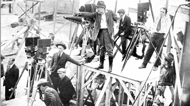 A black & white photograph of Cecil B DeMille directing a scene on top of a lift.