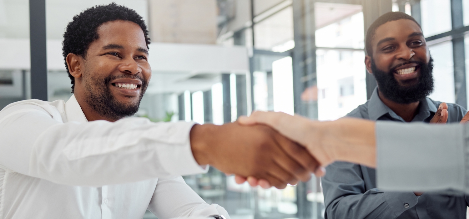A white and black teenage man shaking hands with the director of GOTAP in his office after a conversation about business to business relationship marketing is witnessed by his colleague clapping his hands.