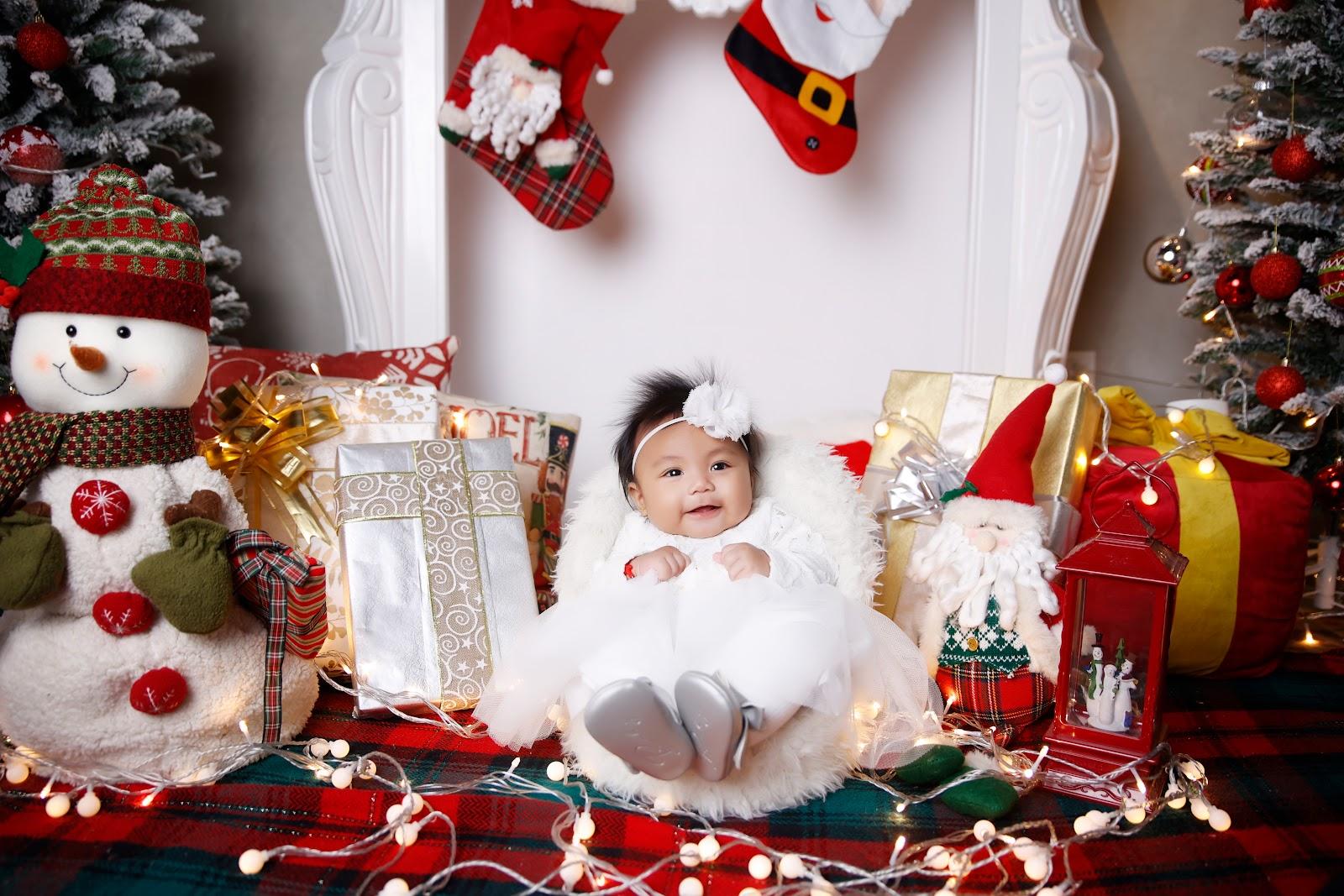 newborn christmas photo idea: baby dressed up in a white dress seated on a sofa bed designed like a manger surrounded by fairy lgihts