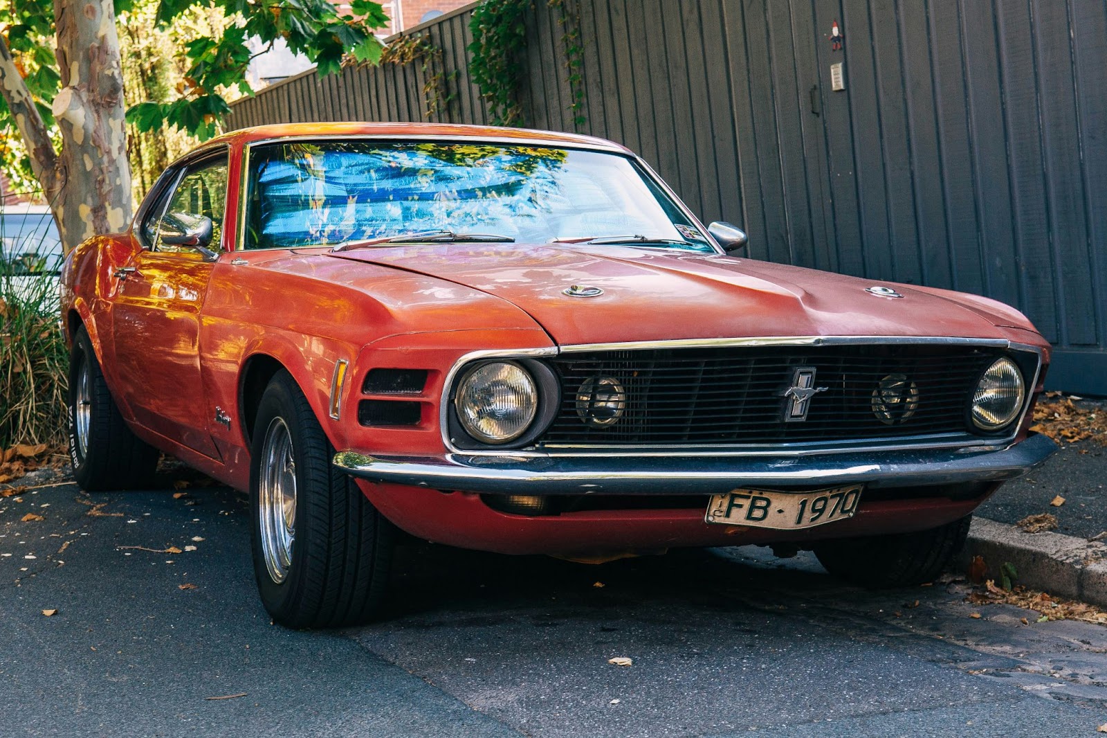 a used orange-red mustang parked alongside a driveway
