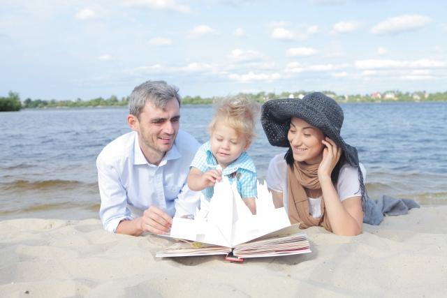 海岸で子供と両親が絵本を読んでいる写真