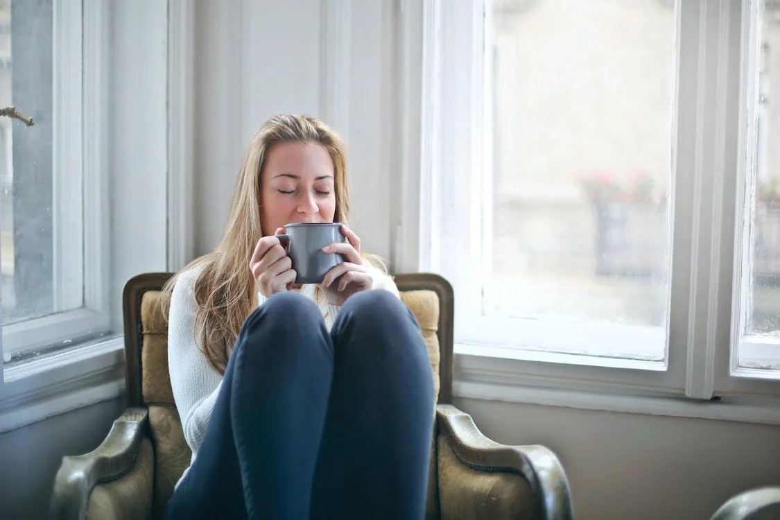 Woman sitting in chair with knees up drinking tea and practicing tea resolutions