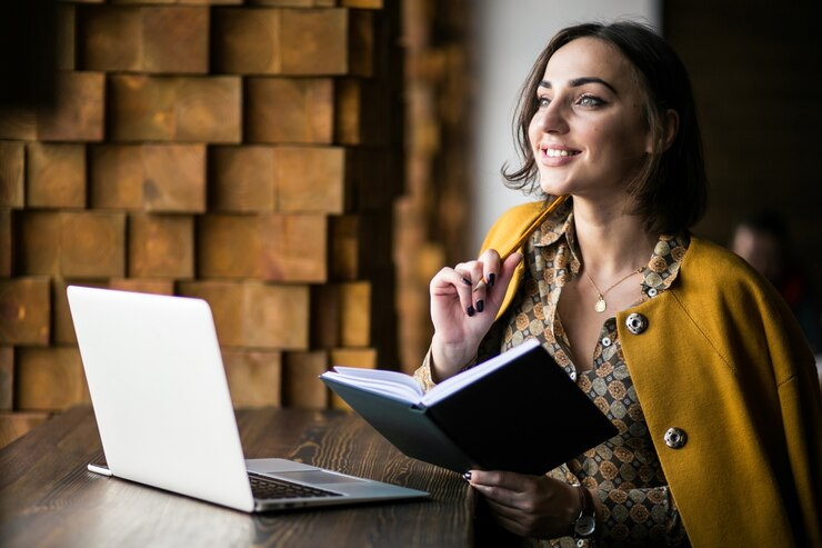 Woman smiling while holding a book and reading women lifestyle blogs on her laptop