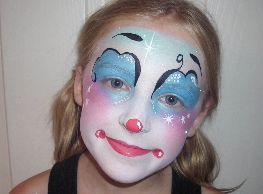 A young girl with a cheerful expression, wearing face paint resembling a clown.