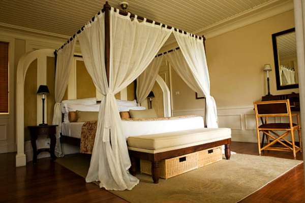 Canopy bed frame with white curtains in a bed room.