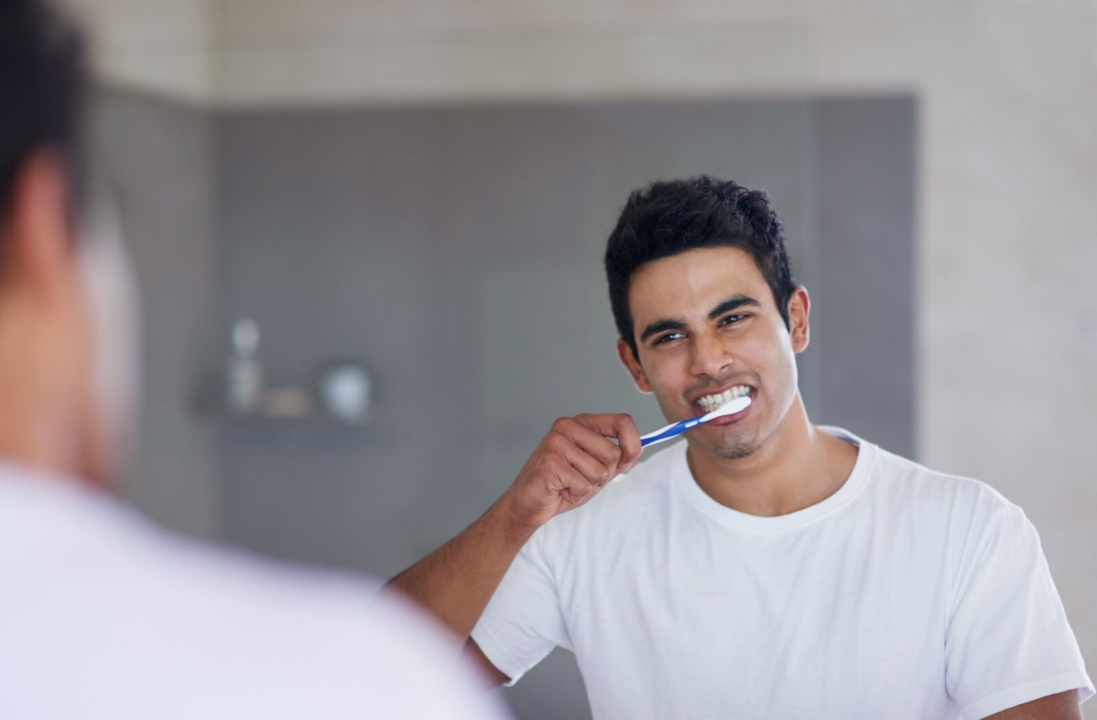 A man brushing his teeth in front of a large bathroom mirror.