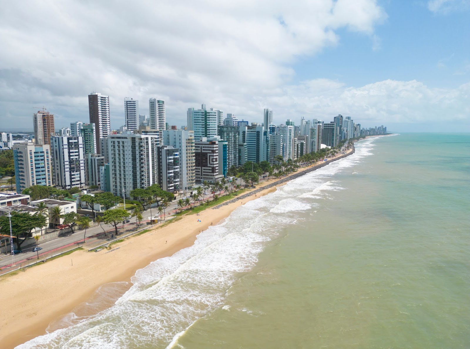Praia de Candeias, com diversos prédios que vão do lado esquerdo ao meio da foto, faixa de areia extensa e mar com águas cristalinas