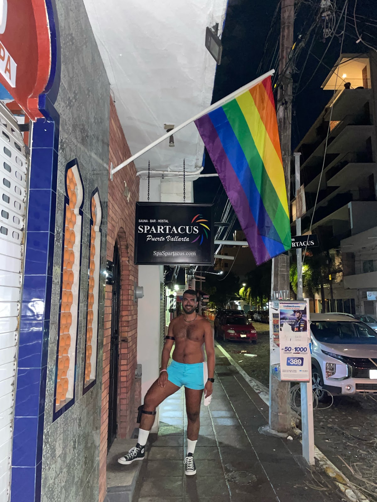 gay male shirtless standing in puerto vallarta streets wearing baby blue shorts standing outside of the spartacus gay male bathhouse for fucking