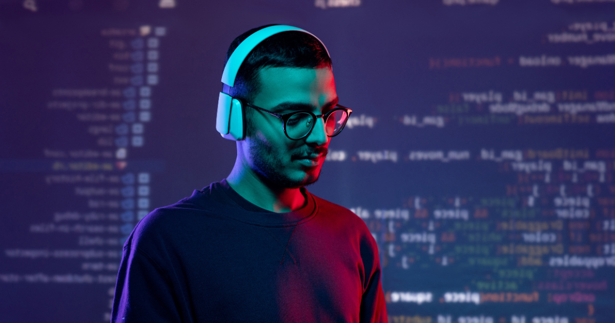 A man with headphones on standing in front of a background full of written code. 
