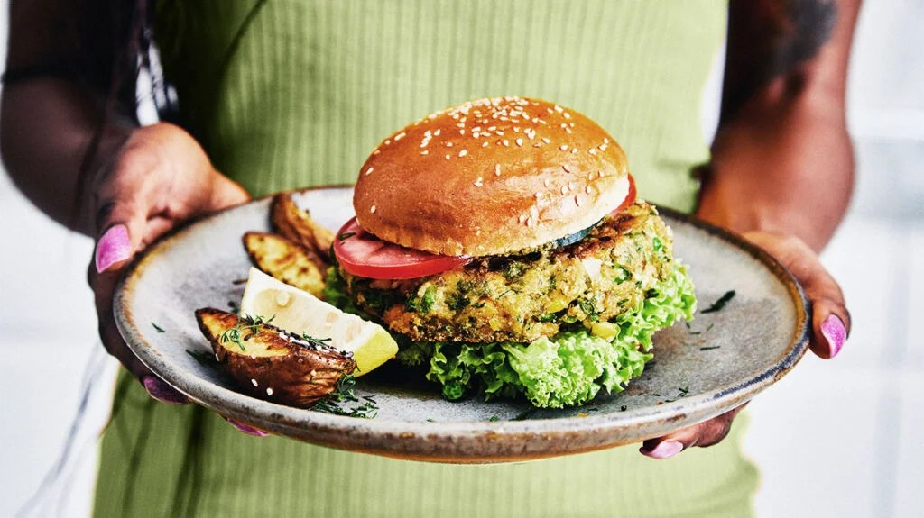 A person holding a vegan burger on a plate