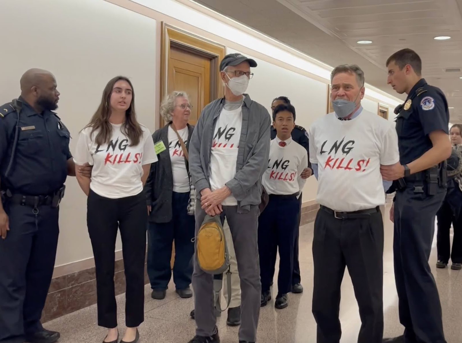 A group of activists wearing shirts that say 'LNG Kills!' are handcuffed by police