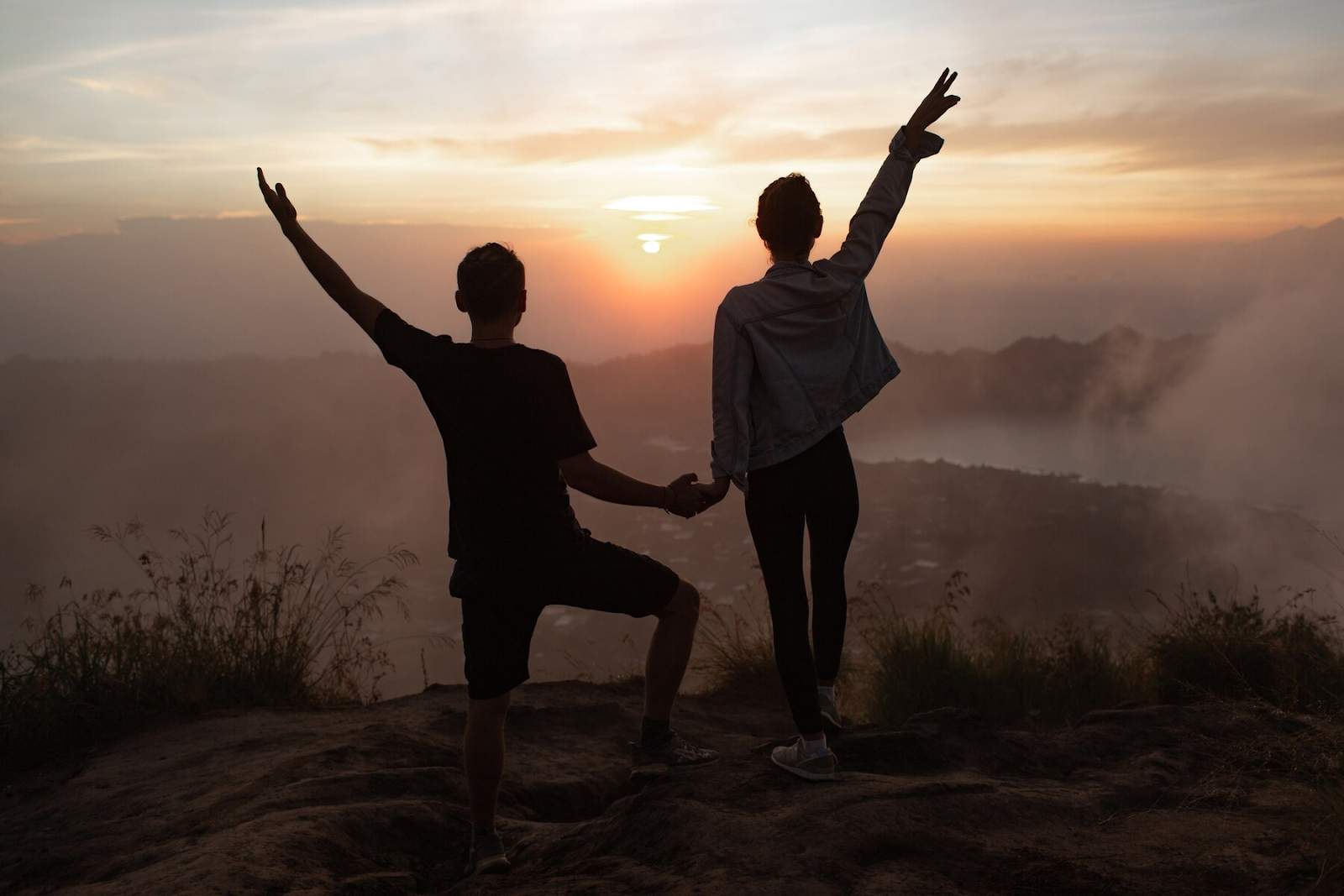 A couple holding hands at dawn on a hill.