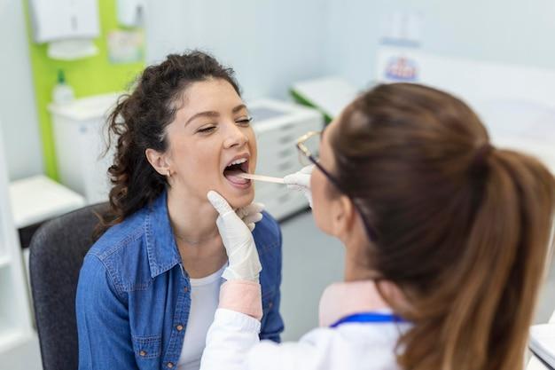 Paciente do sexo feminino abrindo a boca para o médico olhar em sua garganta otorrinolaringologista examina dor de garganta do paciente